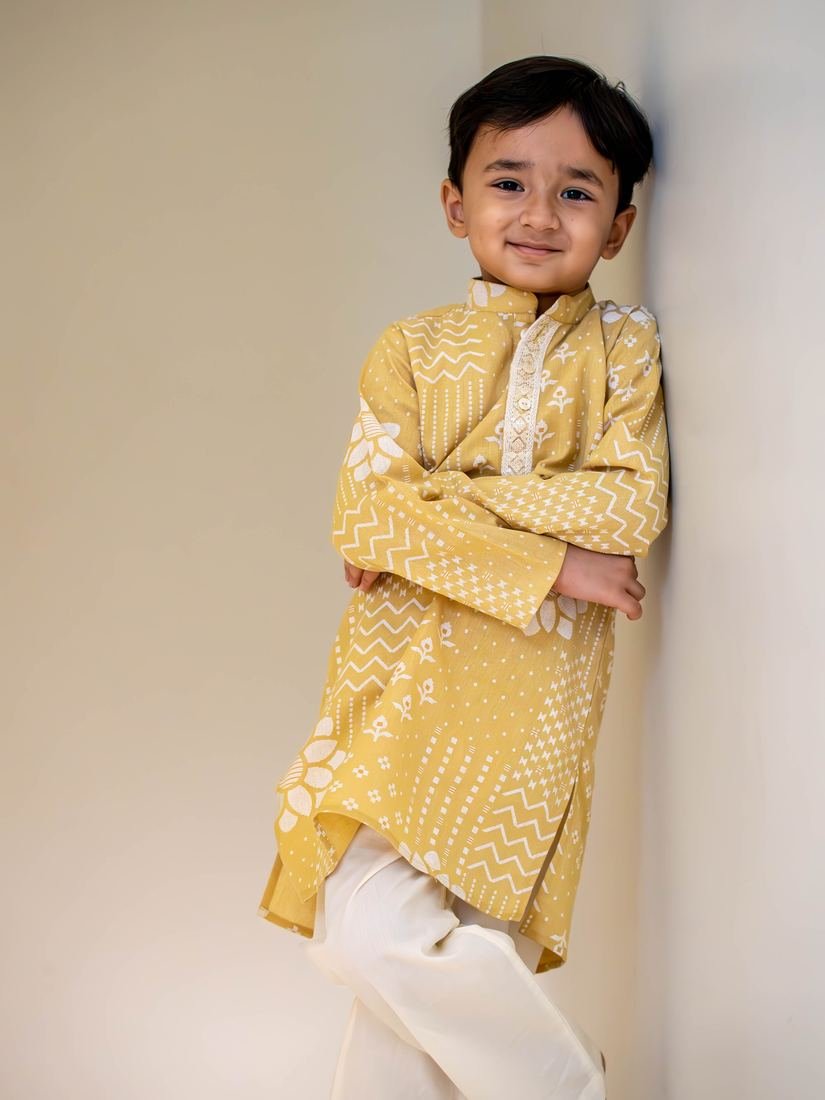 Boy in a yellow kurta leaning against a wall
