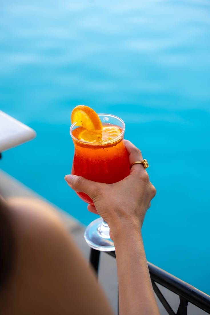Orange cocktail held over a blue lake